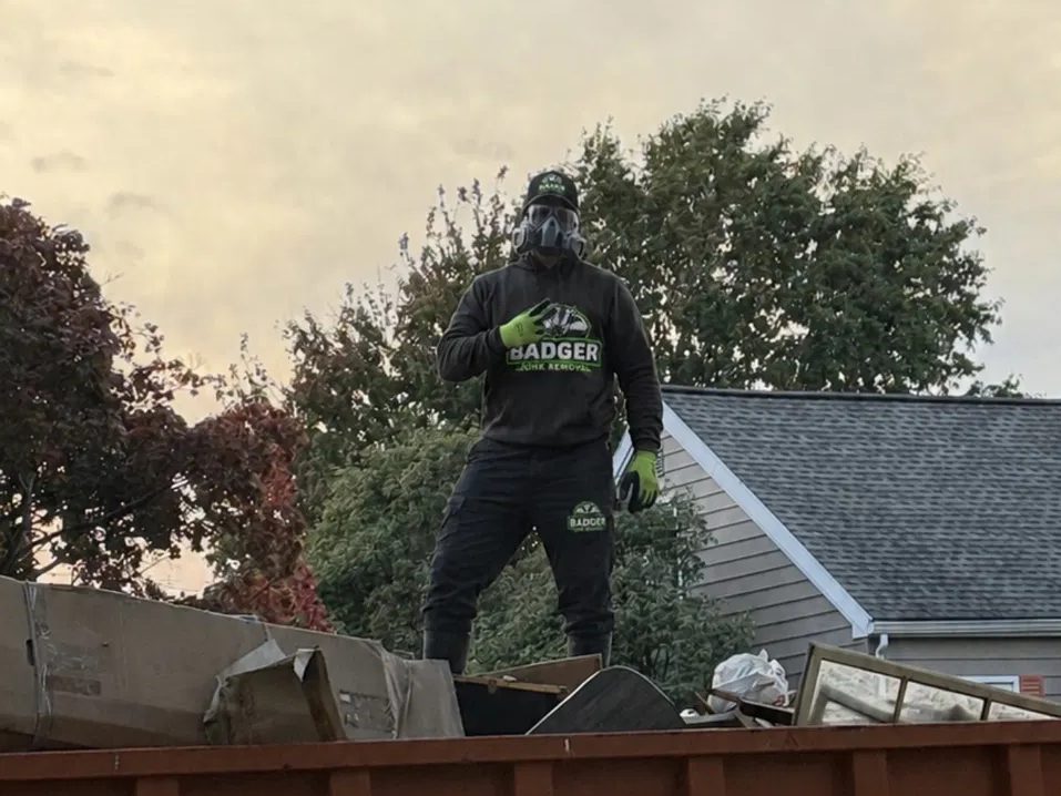 Badger Junk Removal crew member on top of a fully loaded dumpster